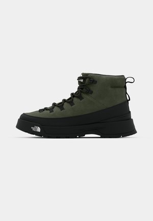 Botte de randonnée en suede verte avec semelle en caoutchouc noire, devant à lacets et détails texturés ; présente un logo sur le côté et une languette à l'arrière.