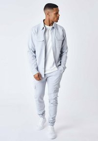 Ljust grå skjortjacka med två bröstfickor, matchad med byxor i cargo-modell och vita sneakers. Slät tyg med en åtsittande design.
