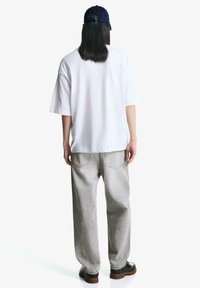 Hvid kortærmet t-shirt parret med lysegrå, løstsiddende jeans og sorte sko. En mørkeblå hat bæres.