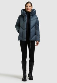 Giacca blu navy imbottita con colletto alto, caratterizzata da pannelli trapuntati diagonali e una cerniera frontale. Indossata con leggings neri e stivali al ginocchio.