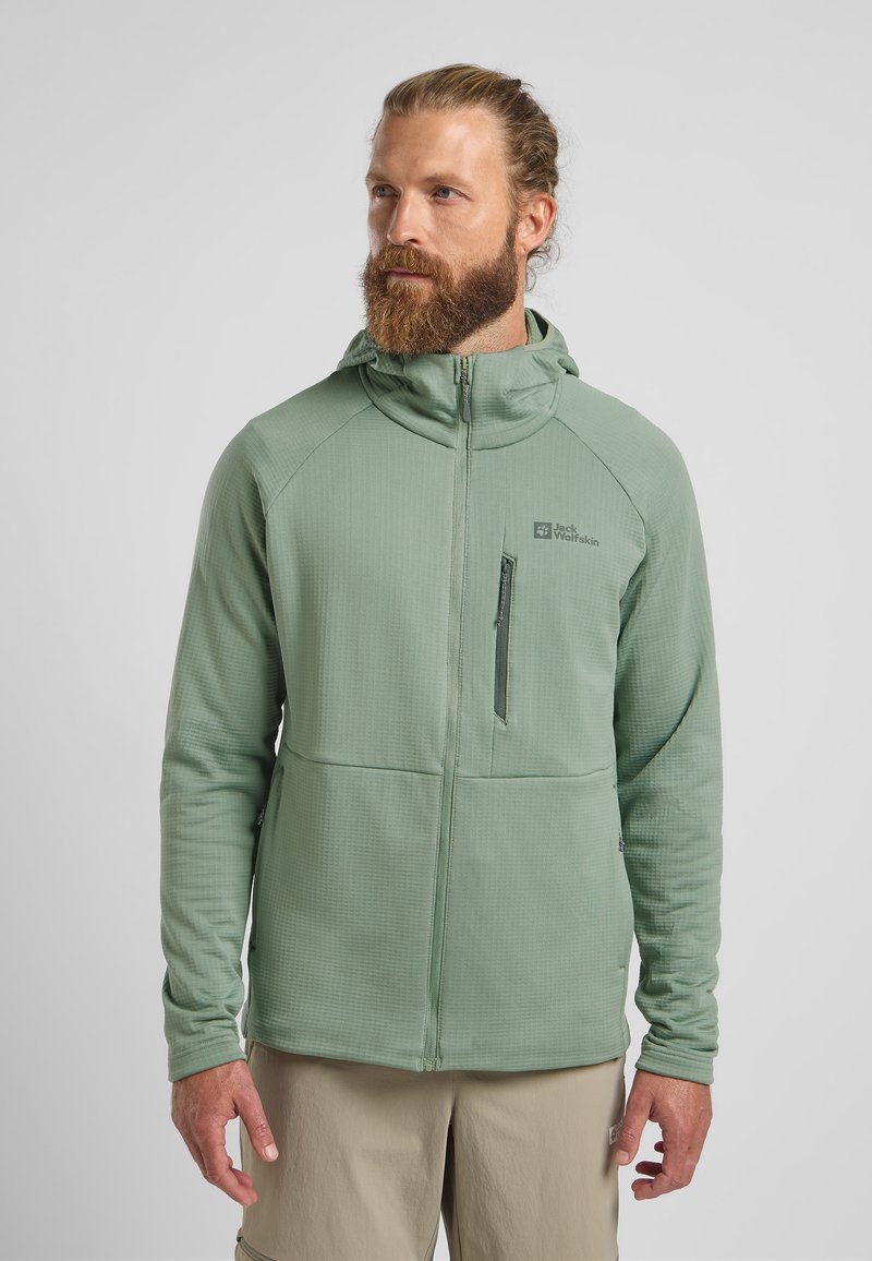 Giacca zip-up verde chiaro con tessuto testurizzato, cappuccio e taschino sul petto. Presenta un logo sul lato sinistro e maniche attillate.