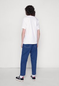 White short-sleeve t-shirt paired with blue loose-fitting denim jeans and black sneakers featuring red accents. Back view, flat background.