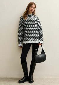 Zwart-witte houndstooth trui met een hoge nek. Zwarte leggings, kniehoge zwarte laarzen en een kleine zwarte handtas maken de outfit compleet.