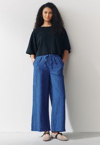 T-shirt noir court avec manches larges, associé à un pantalon ample bleu à motif à carreaux, doté d'un cordon de serrage ajustable et de poches.