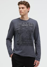 Langärmliges graues Hemd mit bedrucktem Text und Grafiken. Besitzt einen runden Ausschnitt und ein strukturiertes Material. Genähte Akzente an den Schultern.