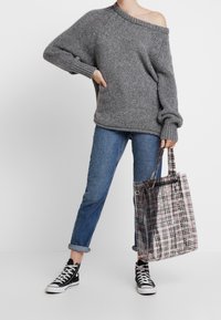 Maglione grigio a spalle scoperte, vestibilità ampia, maniche lunghe; abbinato a jeans blu risvoltati e sneakers nere alte. Porta una borsa a tracolla a quadri.