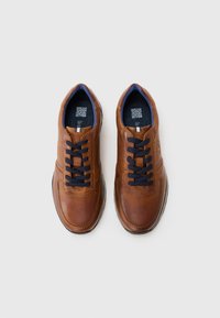Ein Paar braune Leder-Schnürschuhe mit schwarzen Schnürsenkeln und blauer Innenausstattung, von oben auf einem weißen Hintergrund präsentiert.