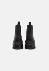 Botines negros hasta el tobillo con un acabado suave y mate, paneles laterales elásticos y una suela gruesa y robusta. "KARL" grabado en el talón.