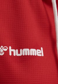 Rood gestructureerd sportstof met een wit "hummel" logo en accentdetails aan de linkerkant. Bovenaan is een witte trekkoord zichtbaar.