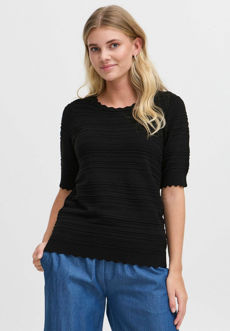 Haut noir texturé à manches courtes, avec un col et un ourlet en forme de vagues. Associé à un pantalon en denim ample.