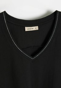 Czarny T-shirt z dekoltem w serek o miękkiej fakturze, z kontrastującym białym szwem wzdłuż dekoltu. Metka z napisem "diverse S".
