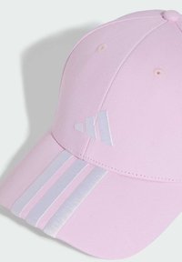 Pink baseball cap with a curved brim, made of textured fabric. Features white stripes and logo accents on the front and sides.