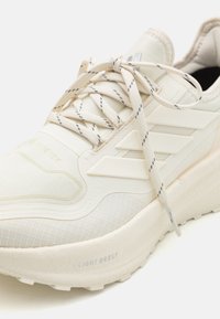 Bijela tenisica koja sadrži GORE-TEX materijal, teksturirani mrežasti gornji dio, dizajn s tri pruge, ojačan vrh i LIGHT BOOST dno za ublažavanje.