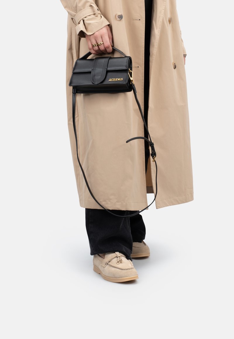 Schwarze Lederhandtasche mit strukturiertem Design, Obergriff und abnehmbarem Gurt. Mit goldfarbener Logo-Detail und Überschlagverschluss.