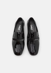 Scarpe slip-on in pelle verniciata nera con dettaglio di una fascia intrecciata sulla parte superiore. Design con punta rotonda e suola piatta. Logo del marchio Gabor visibile.