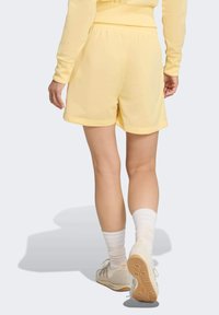 Gele sportbroekjes met een elastische tailleband, een gladde textuur en een losse pasvorm. Draagt met witte kniehoge sokken en lichte sneakers.