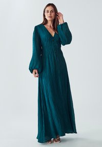 Tyrkysové maxi šaty s dlouhým rukávem, texturovaným materiálem, výstřihem do V a zapínáním na knoflíky. Mají objemové rukávy a splývavou siluetu.
