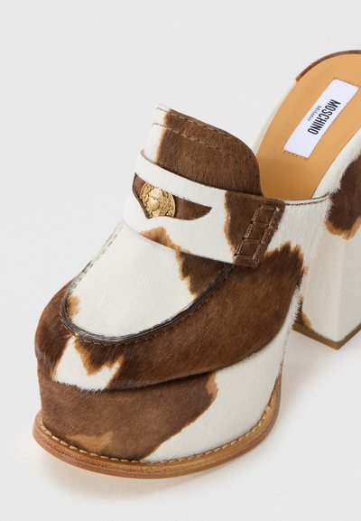 Muli din piele de vacă maro și alb cu toc gros, detaliu în formă de inimă aurie pe curea și talpă interioară bej etichetată Moschino Milano.