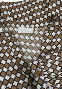 Chemise avec un motif géométrique en diamants marron, blanc et noir, poignet boutonné et étiquette de marque Kaffe visible taille 38.