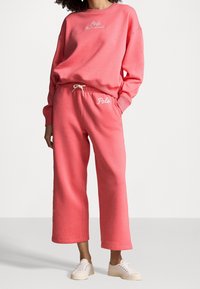 Rosa sweatshirt och matchande byxor i mjukt, strukturerat tyg. Har broderade logotyper, avslappnad passform och dragsko i midjan på byxorna.