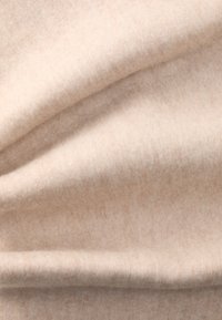 Bežana vunena tkanina s mekim, vlaknastim teksturom. Ima glatke nabore i suptilnu, ujednačenu raspodjelu boje bez vidljivih uzoraka.