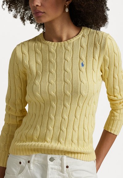 O suéter amarelo em tricô apresenta um decote e punhos canelados, combinado com calças brancas. Pequeno logótipo bordado na parte esquerda do peito.