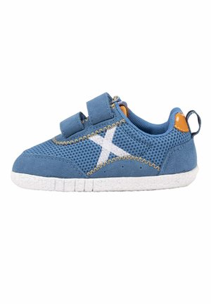 Zapatilla deportiva azul para niño pequeño con suela blanca, logo blanco "X" en el lateral, dos tiras de velcro y detalles naranjas en el talón y la lengüeta.