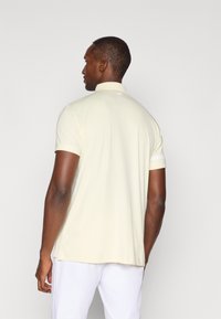 Lichtbeige polo shirt met een geribbelde kraag en korte mouwen, met een klein logo op de achterkant van de hals en zijsplitten aan de onderrand.