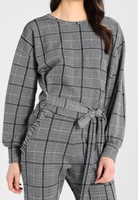 Czarnobiała zestaw loungewear z długimi rękawami, z paskiem w talii i miękką fakturą; wyróżnia się wzorem w kratę i luźnym krojem.