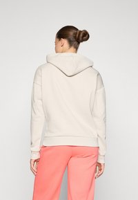 Lichtbeige hoodie met een ontspannen pasvorm, voorzien van een kangoeroezak en geribbelde mouwen, gecombineerd met koraalkleurige trainingsbroek.