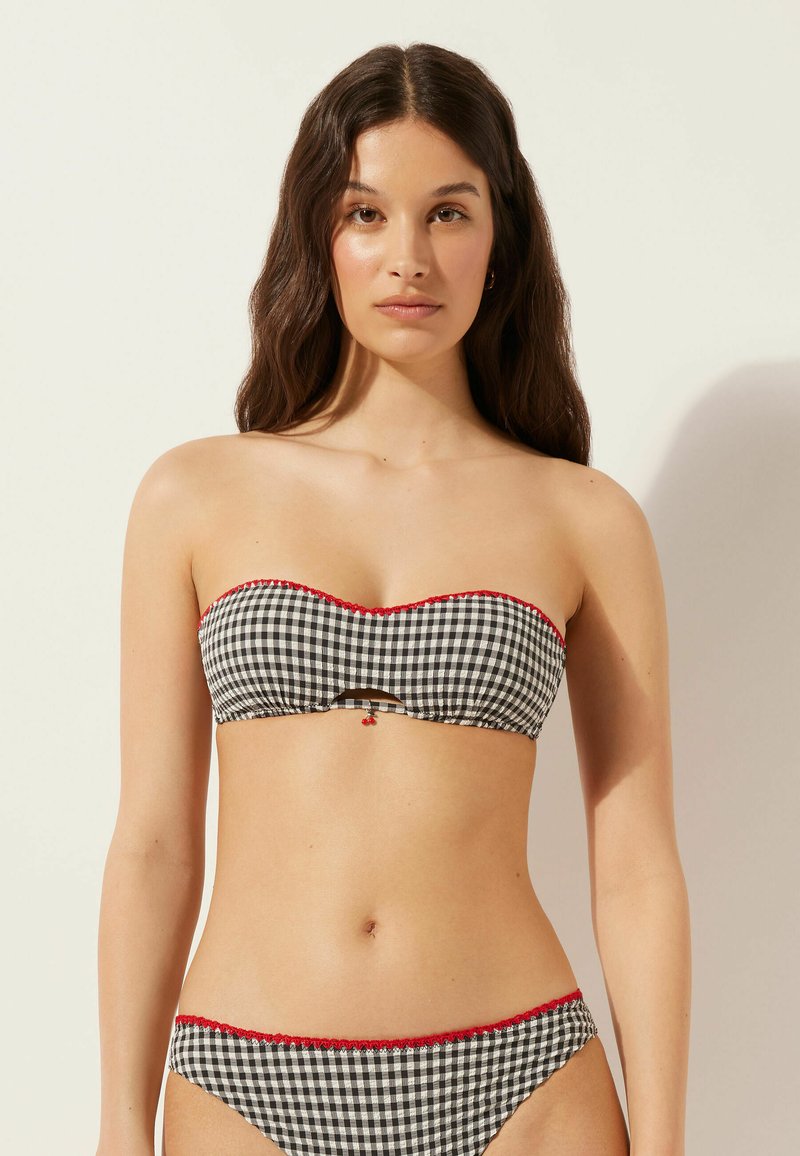 Conjunto de bikini de cuadros en blanco y negro con detalles en rojo. El top sin tirantes presenta un detalle recortado y un pequeño acento. La tela parece suave.