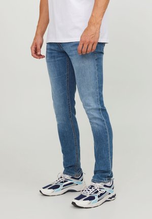 Jeans skinny de mezclilla azul claro con un acabado desgastado, combinados con zapatillas deportivas blancas y marinas con detalles de malla y sintético.