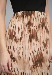 Gros plan sur une personne portant une jupe taille haute avec un imprimé abstrait marron et beige et un haut noir côtelé.