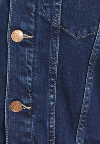 Dark blue denim button-up shirt featuring copper hardware, contrasting tan stitching, and two chest pockets. Texture is smooth with a slight sheen.
