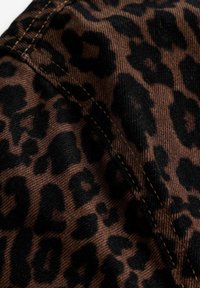 Hnedá látka s čiernym leopardím vzorom, so zreteľným prešívaním. Textúra pôsobí hladko s kvalitým pripomínajúcim dením.