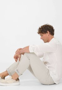 Lichtgewicht witte button-up shirt en beige broek met opgerolde mouwen, gecombineerd met roomkleurige sneakers, zittend tegen een eenvoudig witte achtergrond.