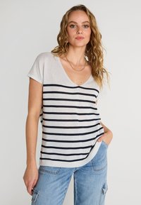 Suéter ligero de rayas beige y azul marino con escote en V, mangas cortas y corte relajado, combinado con pantalones cargo de mezclilla.