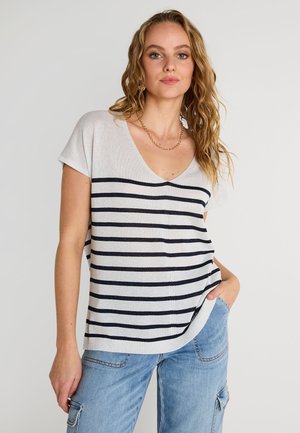 Suéter ligero de rayas beige y azul marino con escote en V, mangas cortas y corte relajado, combinado con pantalones cargo de mezclilla.