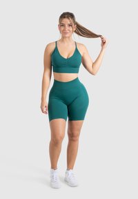 Conjunto atlético en color azul verdoso que incluye una camiseta ajustada de crop con escote redondo y pantalones cortos de talle alto a juego. El material parece suave y elástico.