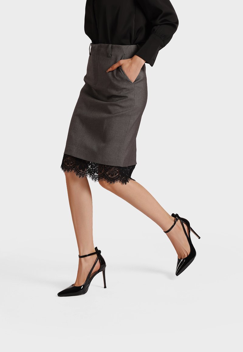 Gonna a matita grigia con bordo in pizzo all'orlo e tasche laterali, abbinata a scarpe con tacco alto in vernice nera con cinturini alla caviglia.