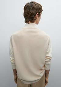 Hellbeiger Strickpullover mit hohem Kragen, geripptem Muster und langen Ärmeln; figurbetontes Design mit leicht abgesenkten Schulternähten.