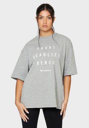 Grijze oversized t-shirt van katoen met een gedurfde witte grafische tekst die "SQUAT DEADLIFT BENCH" onder de hals oplevert.