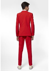 Giacca e pantaloni rosso con un design aderente, tessuto strutturato e una leggera lucentezza. Una camicia bianca è parzialmente visibile al colletto.