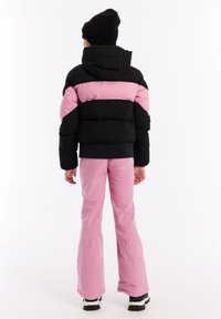 Zwarte en roze pufferjack met capuchon, voorzien van een gevoerd ontwerp, gecombineerd met roze sneeuwbroek en zwarte sneeuwlaarzen.