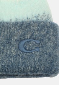 Berretto lavorato a maglia blu con un effetto ombré azzurro. Presenta una finitura texturizzata e pelosa e un logo "C" ricamato di blu scuro sul risvolto.