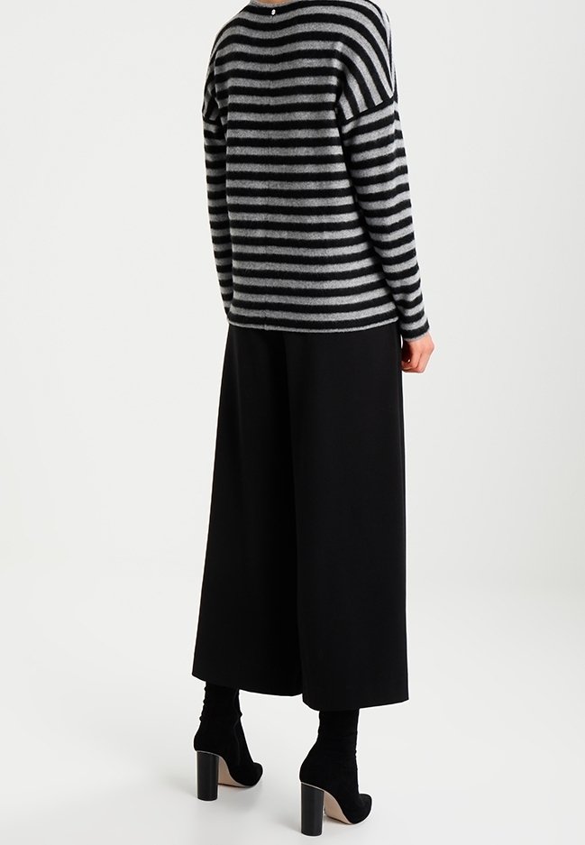 Personne portant un pull rayé gris et noir, un pantalon noir à jambes larges et des bottines noires à talons hauts, vue de dos.