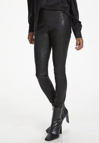 Schwarze Lederleggings, hoch tailliert, glatte Textur, figurbetontes Design, mit seitlichen Nähten versehen und kombiniert mit glänzenden schwarzen Absatz-Ankle Boots.