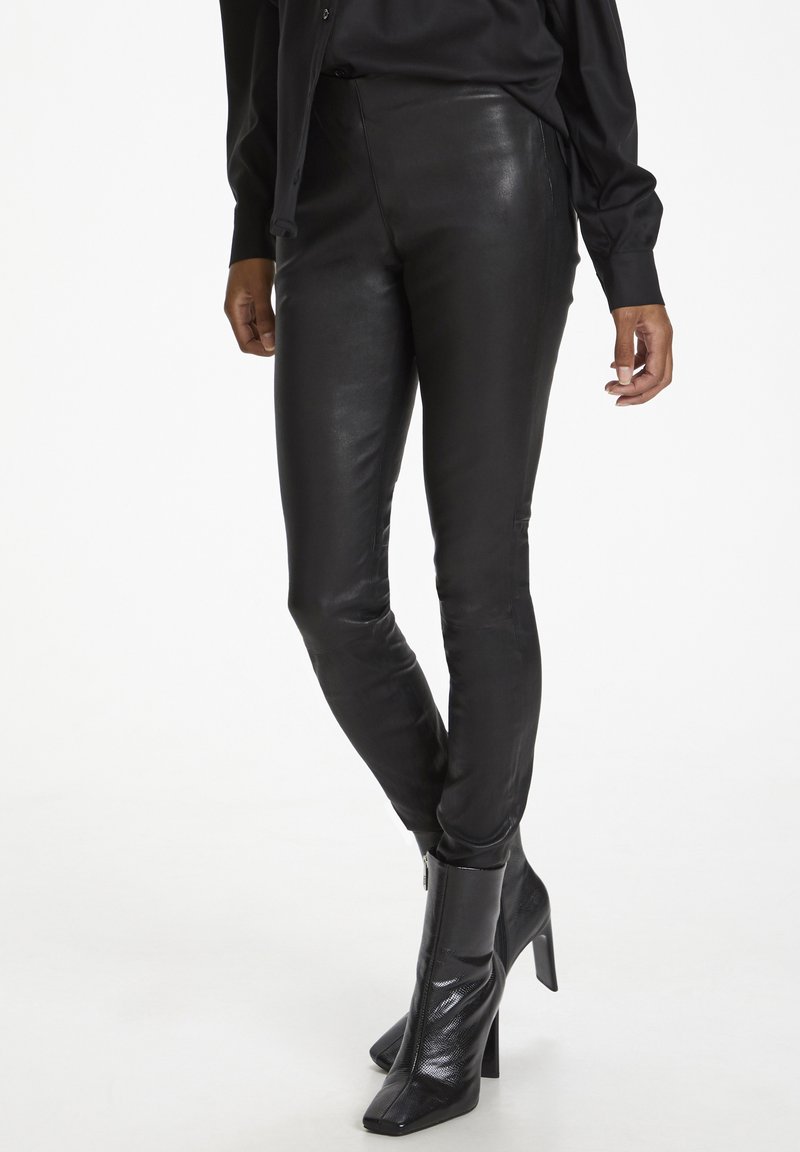 Schwarze Lederleggings, hoch tailliert, glatte Textur, figurbetontes Design, mit seitlichen Nähten versehen und kombiniert mit glänzenden schwarzen Absatz-Ankle Boots.