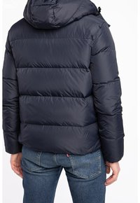 Mörkblå puffjacka med huva, med ett quiltat mönster och elastiska manchetter. Bärs med blå jeans, vilket ger en avslappnad passform.