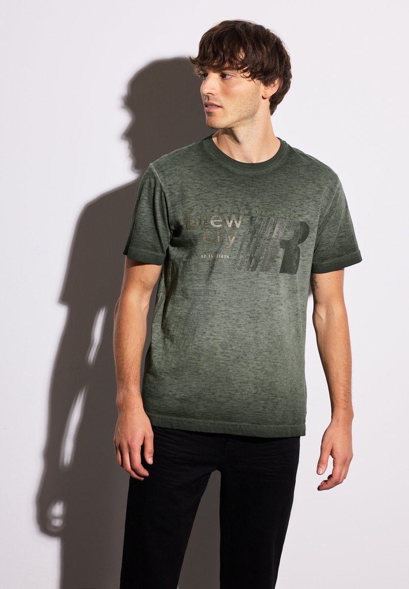 Tmavě zelené bavlněné tričko s texturovaným povrchem. Obsahuje grafický potisk v světlejším odstínu. Kulatý výstřih a krátké rukávy.